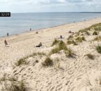 POV view from a surveillance camera overlooking a sandy beach with distant human silhouettes on the Dunes
